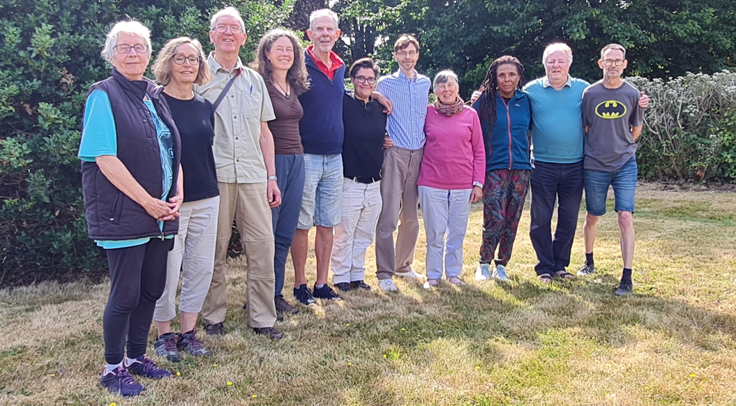 11 Kindlers posing for a group photo in front of hedges and trees in the grounds of the Briary at the August 2026 Retreat